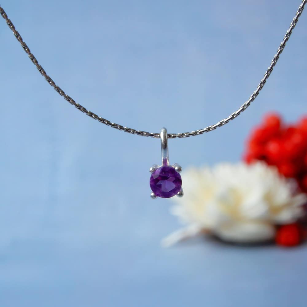 amethyst gemstone silver necklace on blue background with flowers